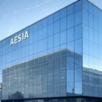 Fachada moderna del edificio sede de la Agencia Española de Supervisión de la Inteligencia Artificial (AESIA) en La Coruña, con reflejos en vidrio.