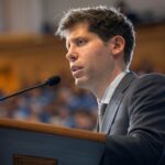 Sam Altman, CEO de OpenAI, hablando en un podio durante un evento sobre inteligencia artificial. La imagen representa el contexto del debate OpenAI contra DeepSeek y la competencia en el sector de la IA.