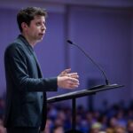 Conferencista en un auditorio hablando sobre Deep Research OpenAI, una herramienta de inteligencia artificial para investigación en línea.