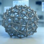 Representación de una estructura molecular avanzada con diseño geométrico metálico, ilustrando la inteligencia artificial en materiales y la arquitectura nanométrica del Carbon Nanolattice en un entorno de laboratorio.