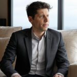 Sam Altman, CEO de OpenAI, sentado en un sofá con traje formal, reflexionando sobre el futuro de la programación impulsado por inteligencia artificial.