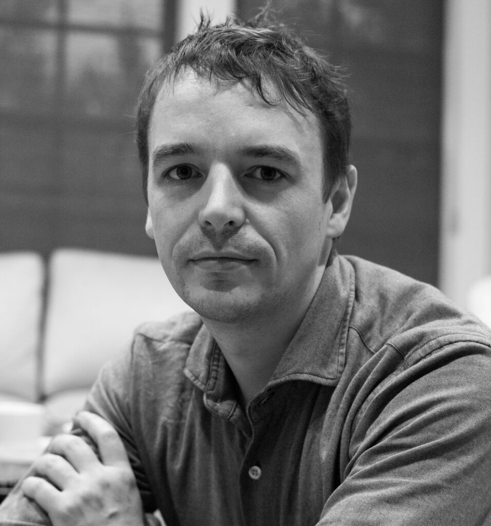 Retrato en blanco y negro de Joscha Bach, pensador alemán, durante una entrevista informal en un entorno interior, con expresión reflexiva.