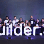Equipo de Builder.ai posando frente al logo iluminado durante un evento corporativo, reflejando la imagen pública antes del escándalo.