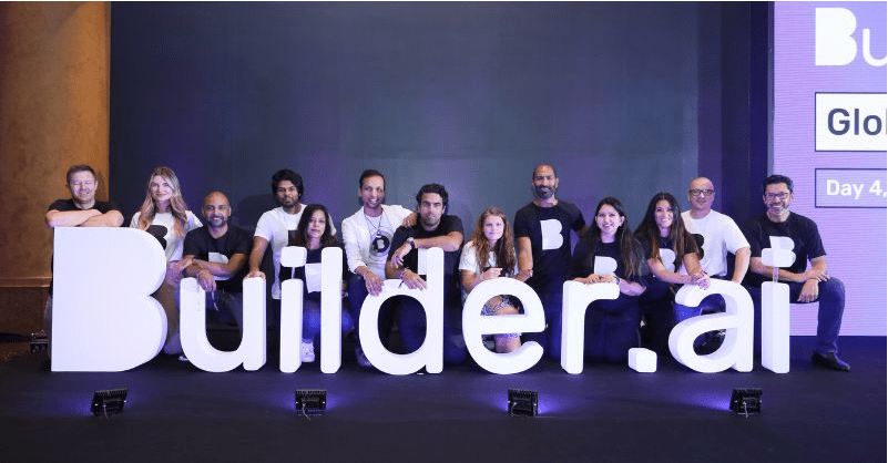 Equipo de Builder.ai posando frente al logo iluminado durante un evento corporativo, reflejando la imagen pública antes del escándalo.